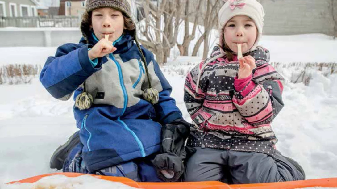 Deux enfants en train de manger de la tire d'érable à l'extérieur.