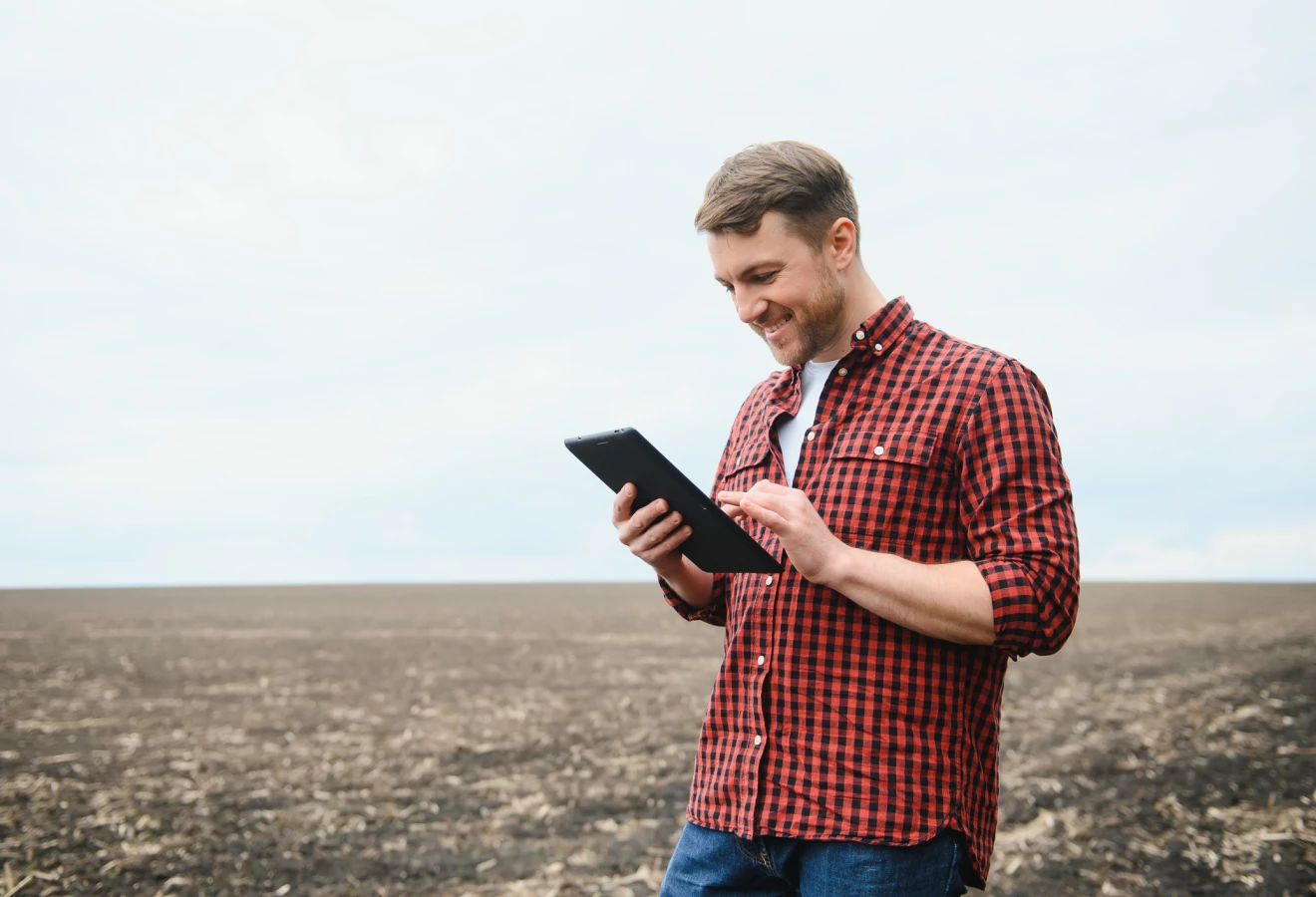 Homme tenant une tablette dans un champ au sol nu