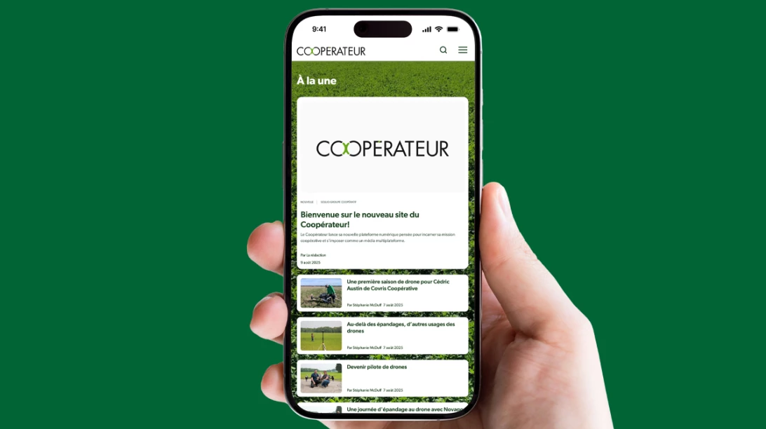 Une main tient un cellulaire sur lequel le site du Coopérateur apparaît