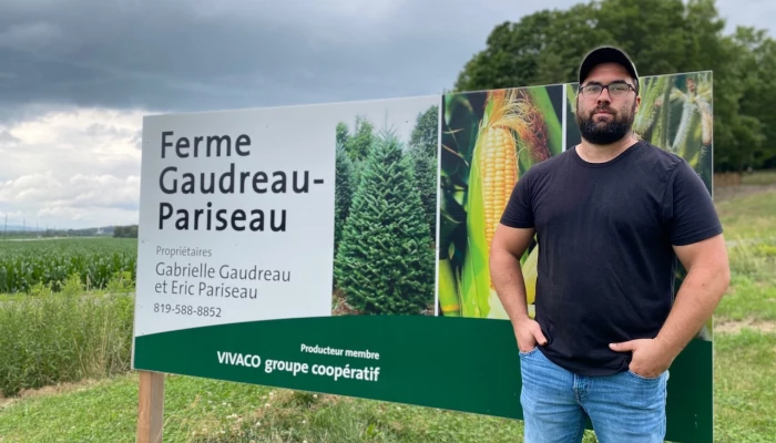 Photo d'Éric Pariseau devant une affiche de la ferme