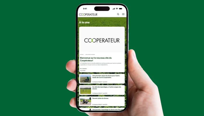 Une main tient un cellulaire sur lequel le site du Coopérateur apparaît
